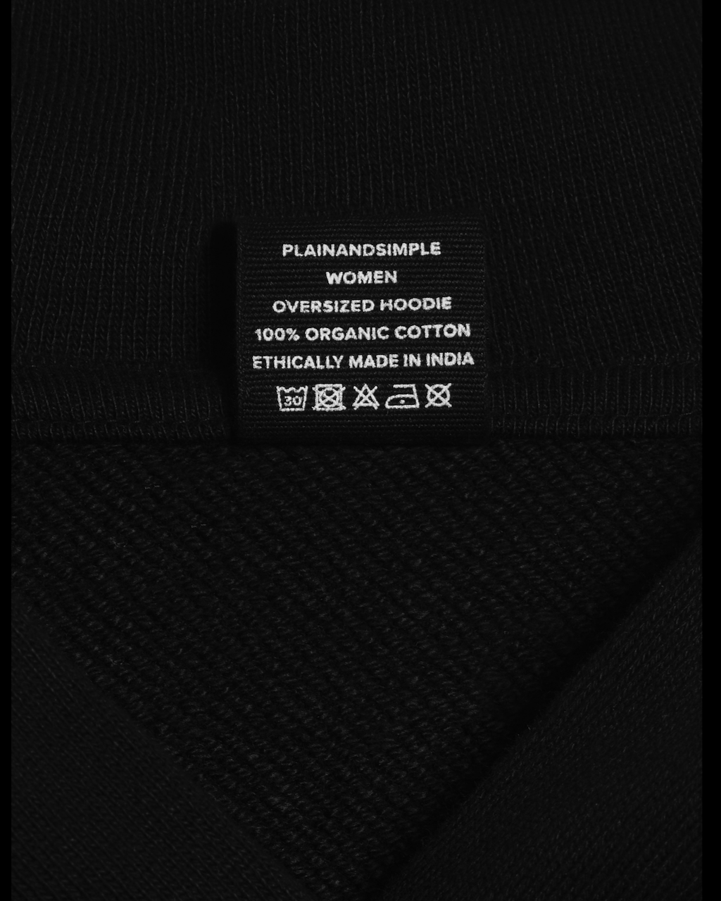 A close up of the neck label in a black, oversized, organic cotton hoodie.