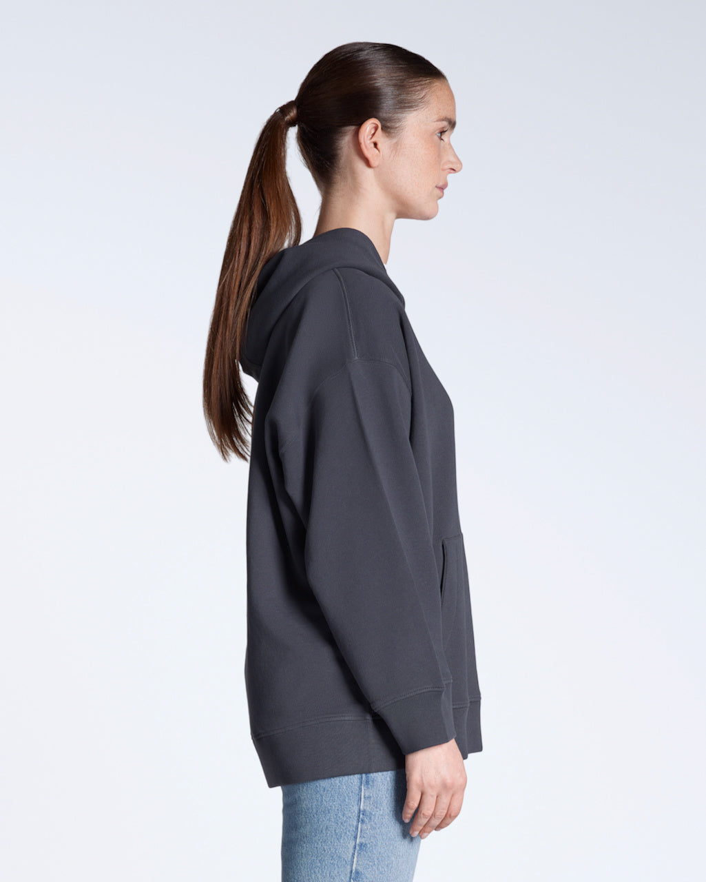 A woman facing side on, modelling a plain dark grey, oversized, organic cotton hoodie.