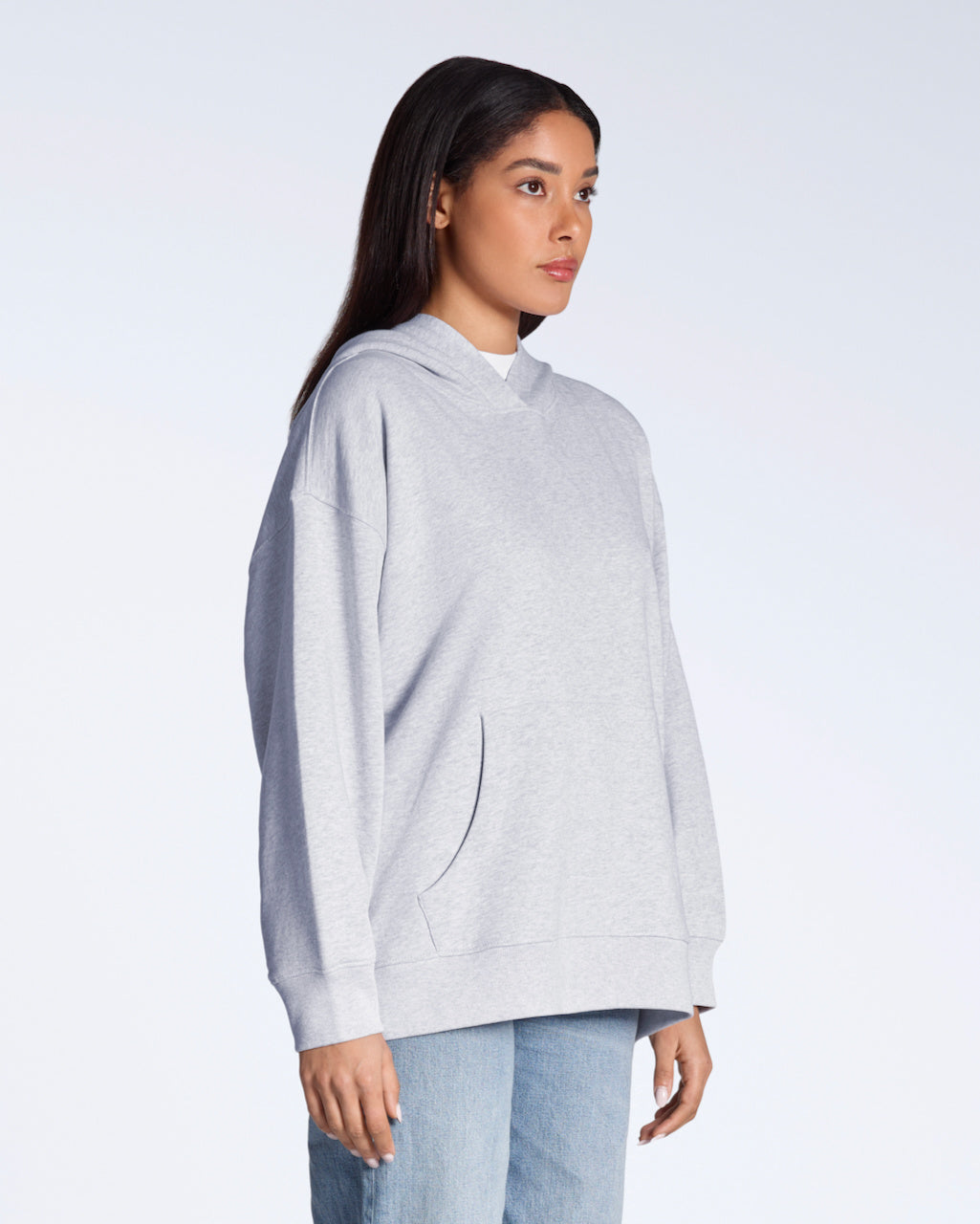 A woman at an angle with her arms by her sides, modelling a plain grey, oversized, organic cotton hoodie.