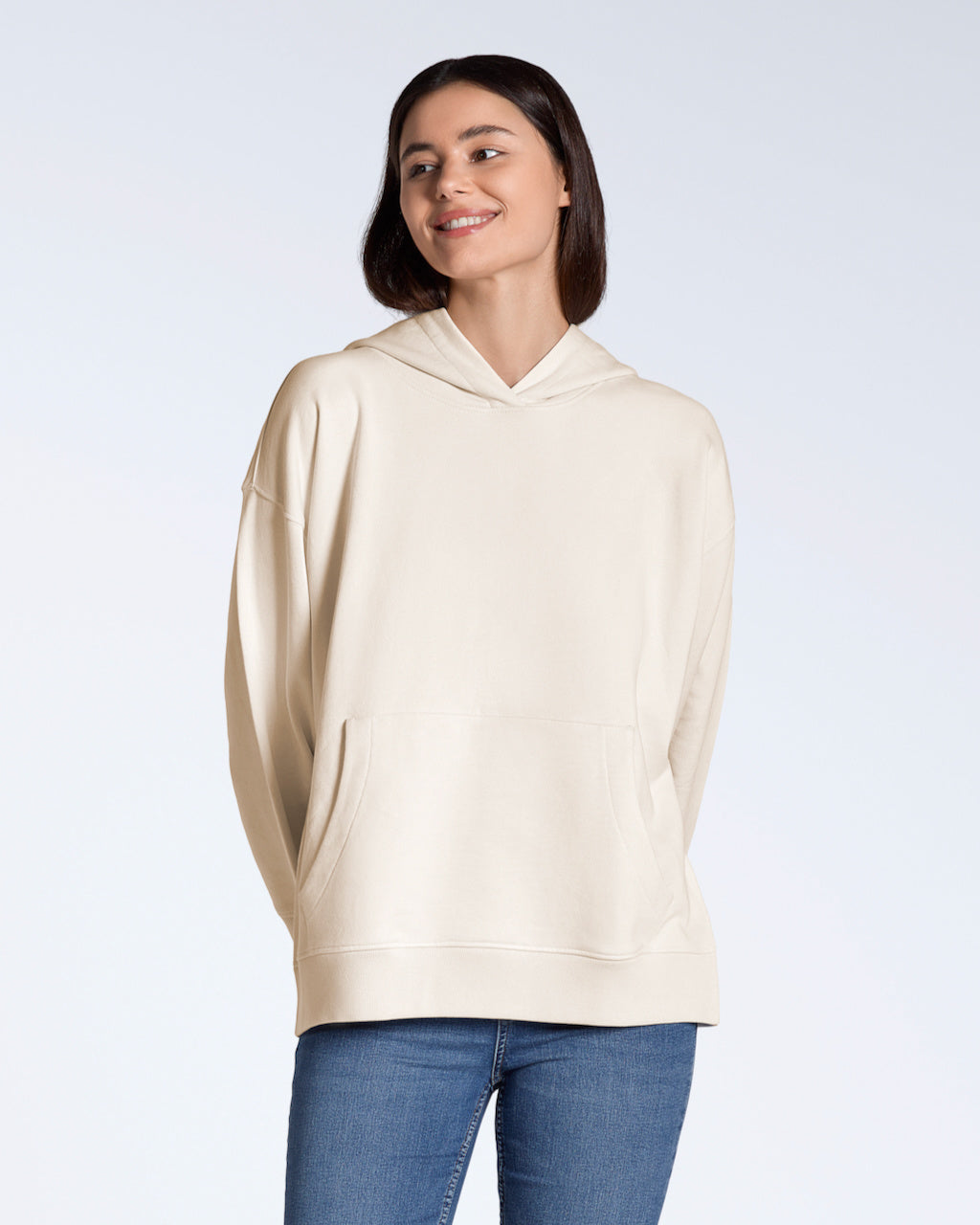 A woman smiling, modelling a plain natural coloured, oversized, organic cotton hoodie.