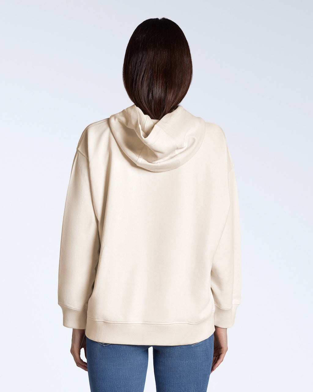 A woman facing away from the camera with her hands by her sides, modelling a natural coloured, oversized, organic cotton hoodie.