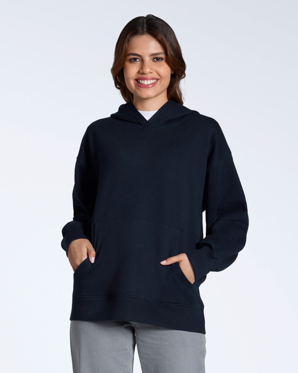 A woman smiling with her hands in her pockets, modelling a plain navy, oversized, organic cotton hoodie.