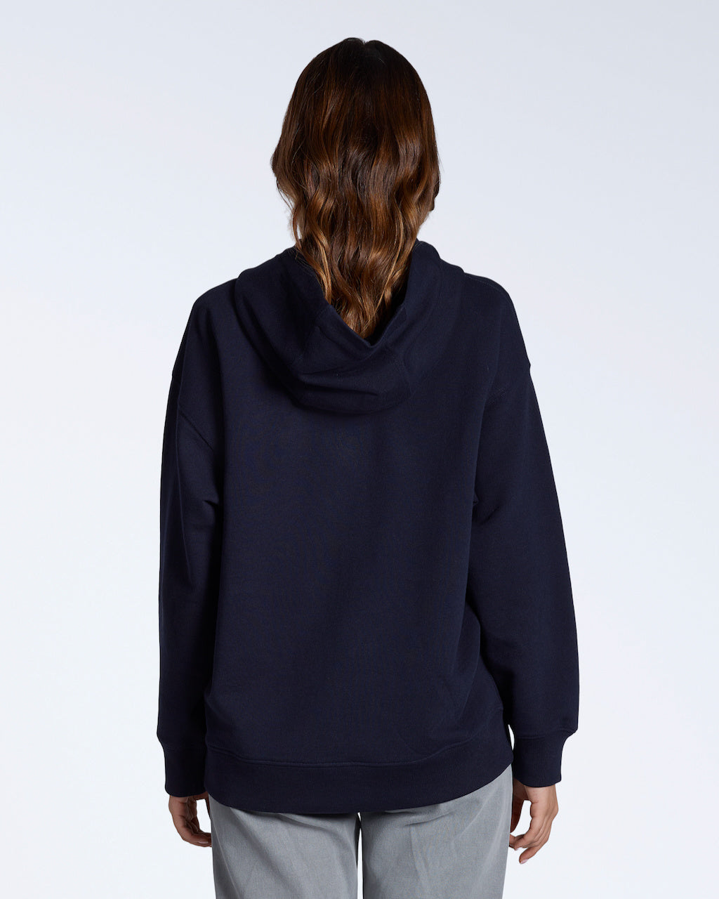A woman facing away from the camera with her hands by her sides, modelling a plain navy, oversized, organic cotton hoodie.