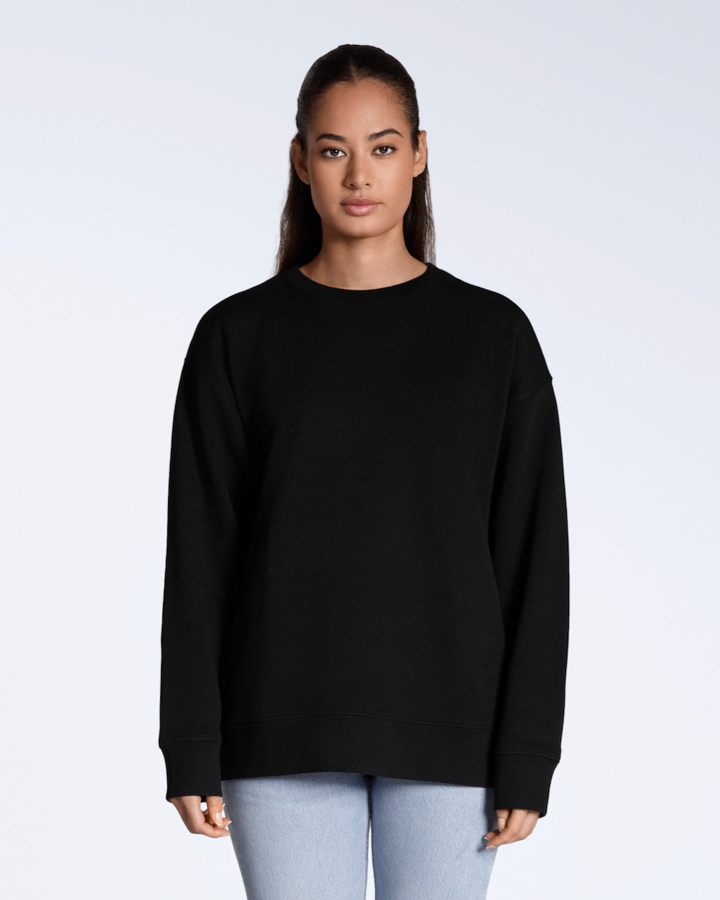 A woman facing front on, looking into the camera with her arms by her side, modelling a plain black, oversized, organic cotton sweatshirt.