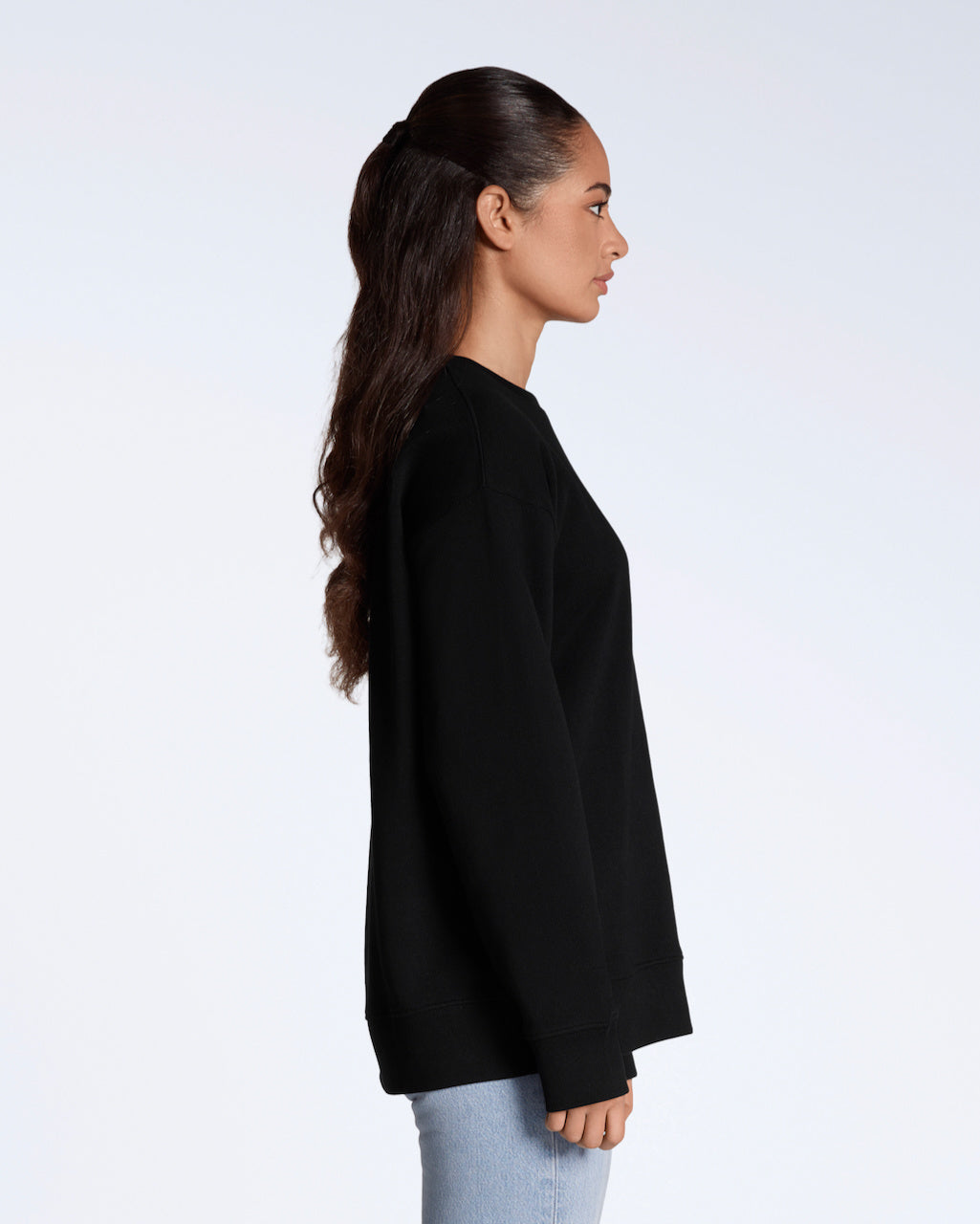 A woman facing side on, with her arms by her side, modelling a plain black, oversized, organic cotton sweatshirt.