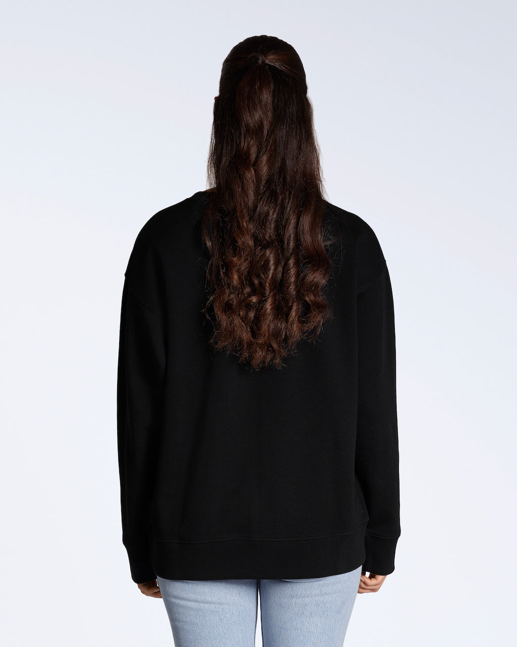 A woman facing away from the camera, modelling a plain black, oversized, organic cotton sweatshirt.