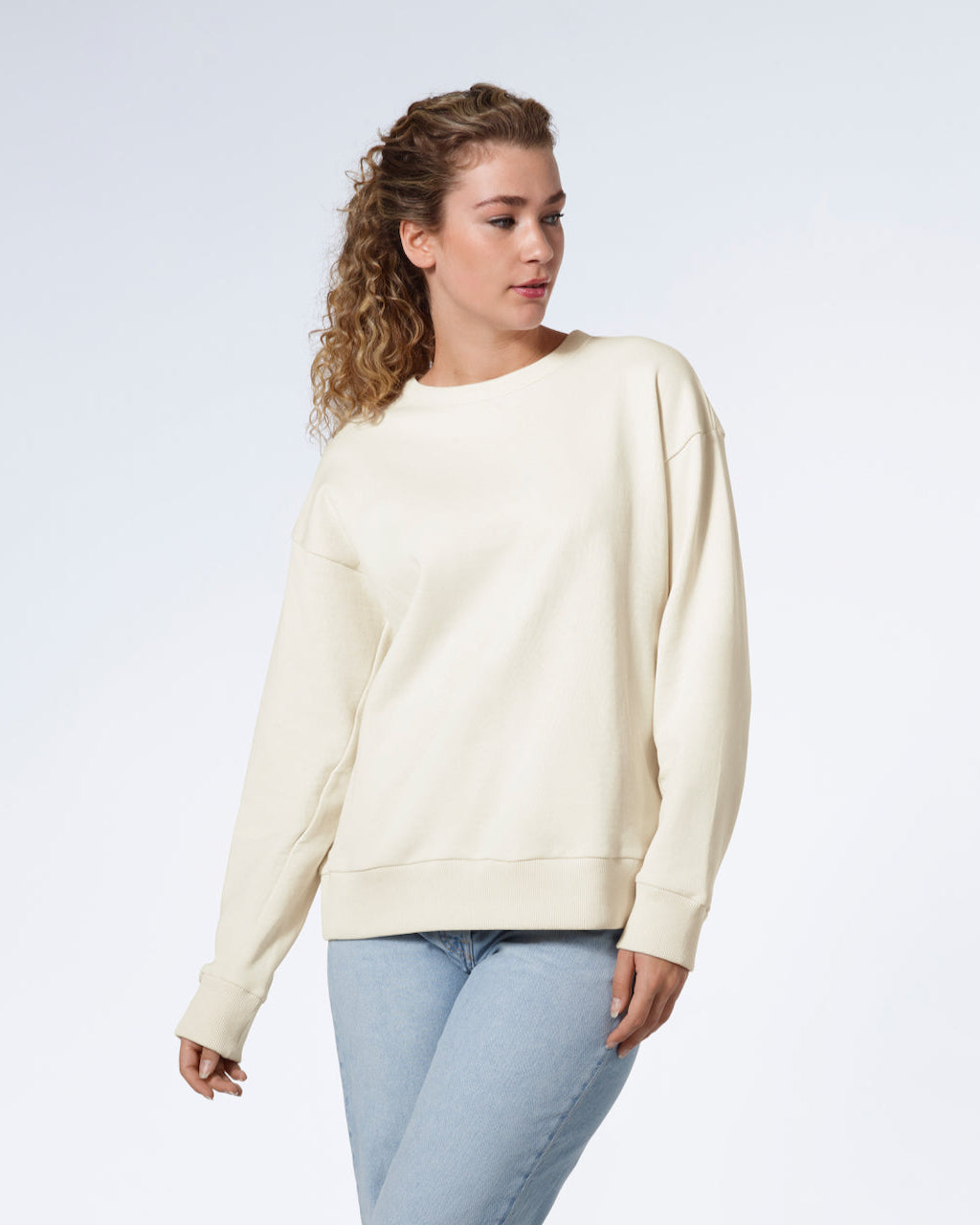 A woman looking away from the camera with her arms by her side, modelling a plain ecru oversized organic cotton sweatshirt.