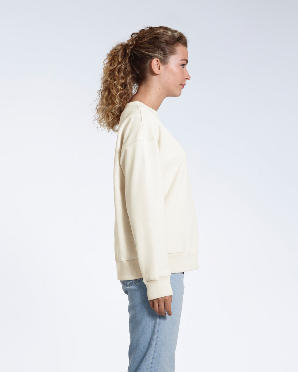A woman facing side on with her arms by her side, modelling a plain ecru oversized organic cotton sweatshirt.