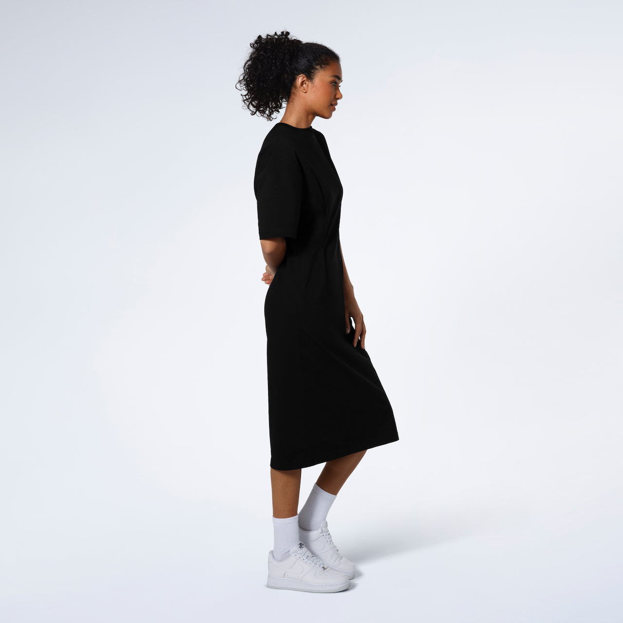 A women standing side on modelling a plain black, organic cotton midi t shirt dress.