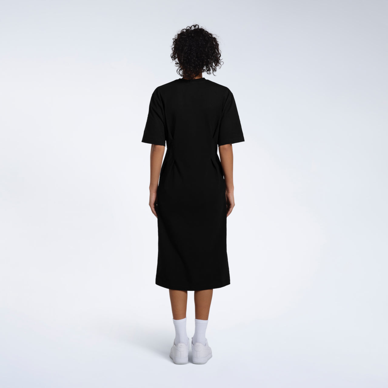 A women facing away from the camera, modelling a plain black, organic cotton midi t shirt dress.