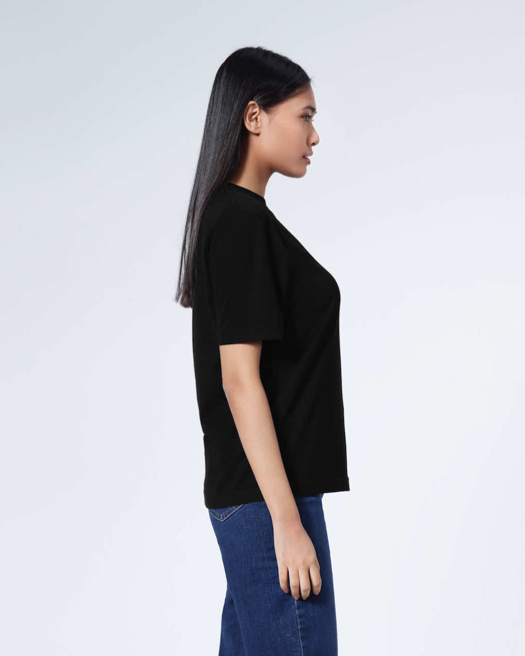 A woman facing side on, modelling a plain black short sleeve organic cotton t shirt.