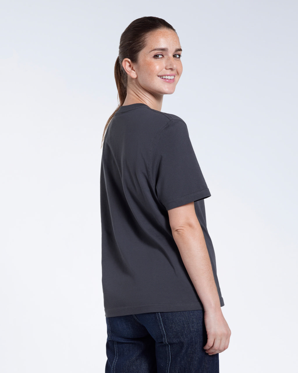 A woman turned towards the camera smiling, modelling a plain dark grey short sleeve organic cotton t shirt.