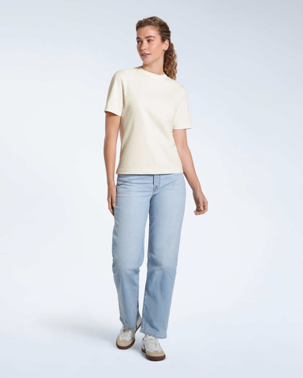 A woman looking away from the camera, modelling an ecru short sleeve organic cotton t shirt.