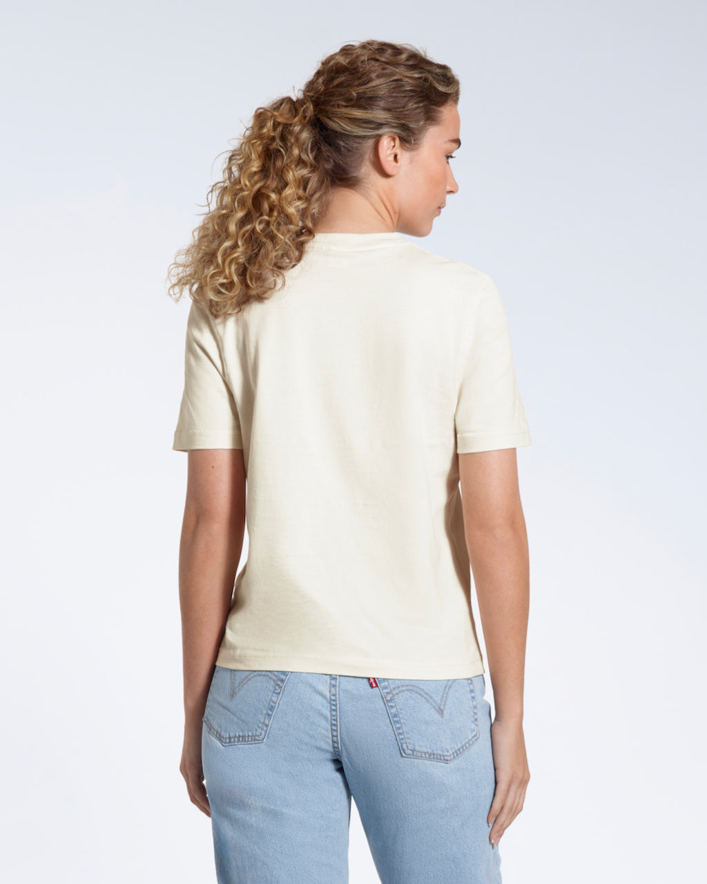 A woman with her back to the camera, modelling a plain ecru short sleeve organic cotton t shirt.