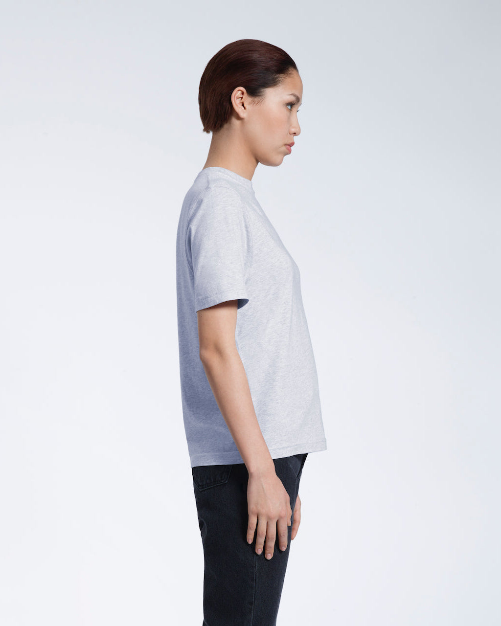 A woman facing side on, modelling a plain grey coloured short sleeve organic cotton t shirt.
