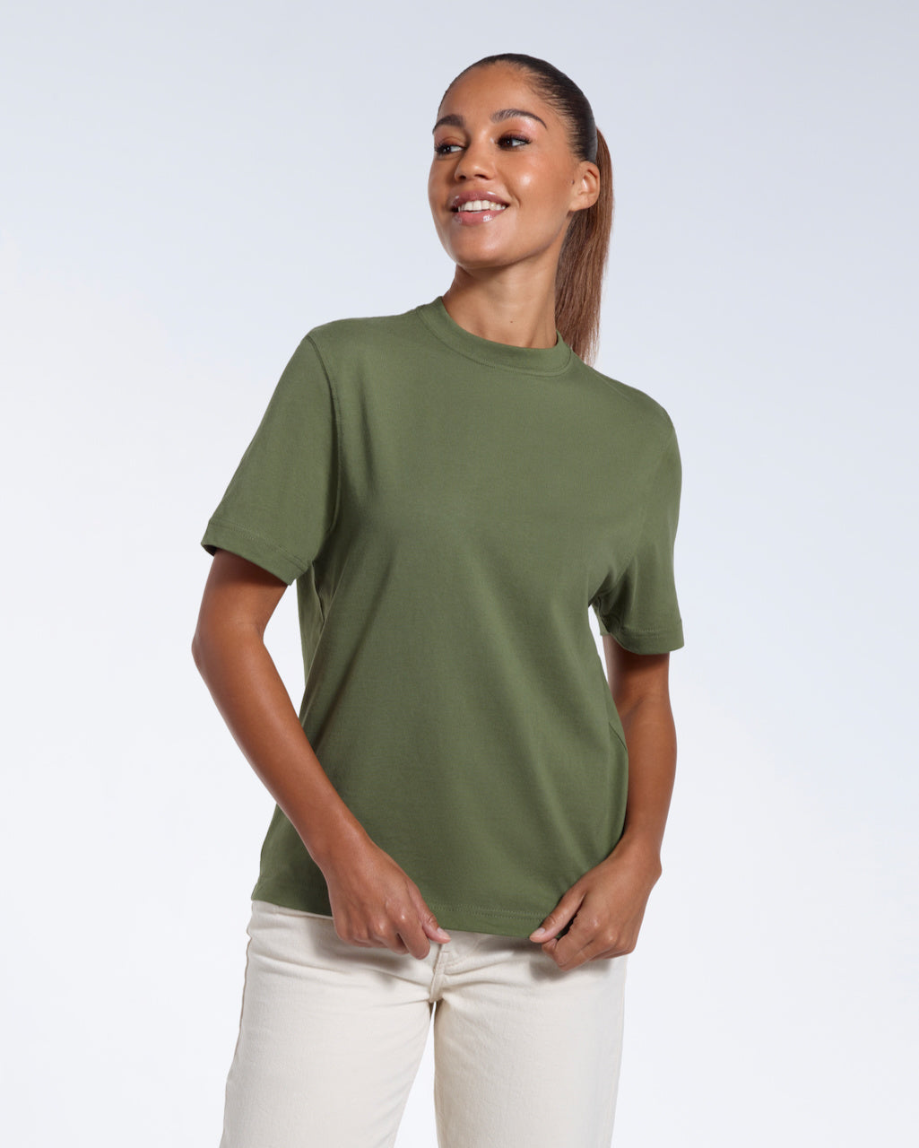 A woman smiling, touching the bottom of her plain khaki green short sleeve organic cotton t shirt.