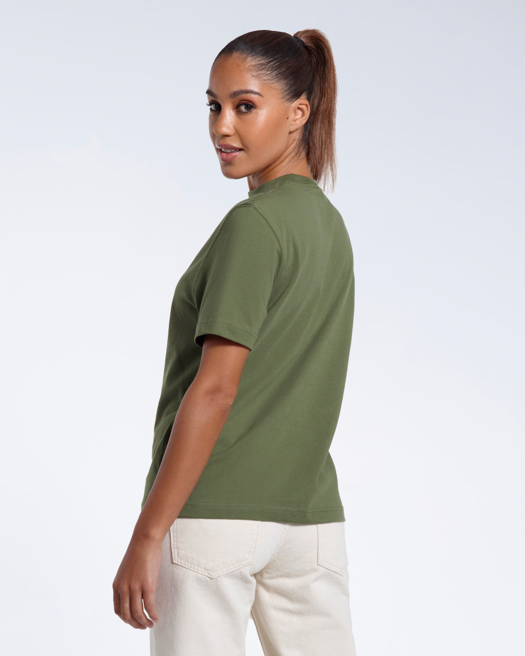 A woman turned towards the camera smiling, modelling a plain khaki green short sleeve organic cotton t shirt.