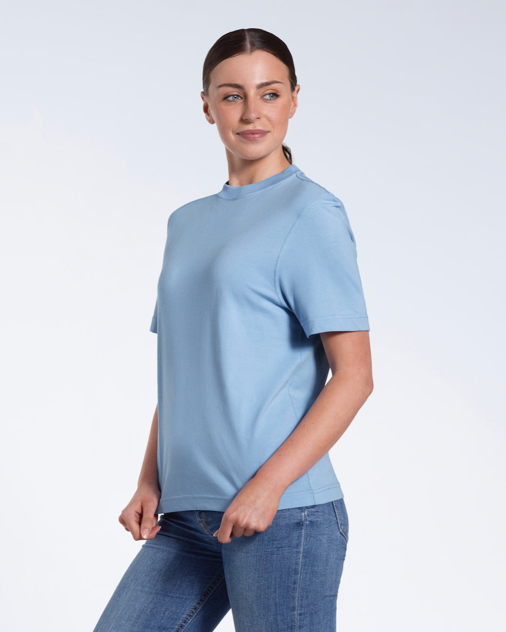 A woman smiling, touching the bottom of her plain blue short sleeve organic cotton t shirt.