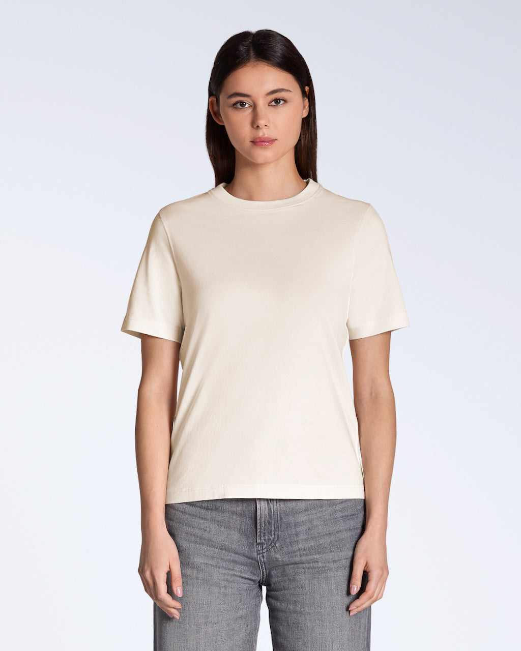 A woman facing front on looking into the camera, modelling a plain natural coloured, organic cotton t shirt.