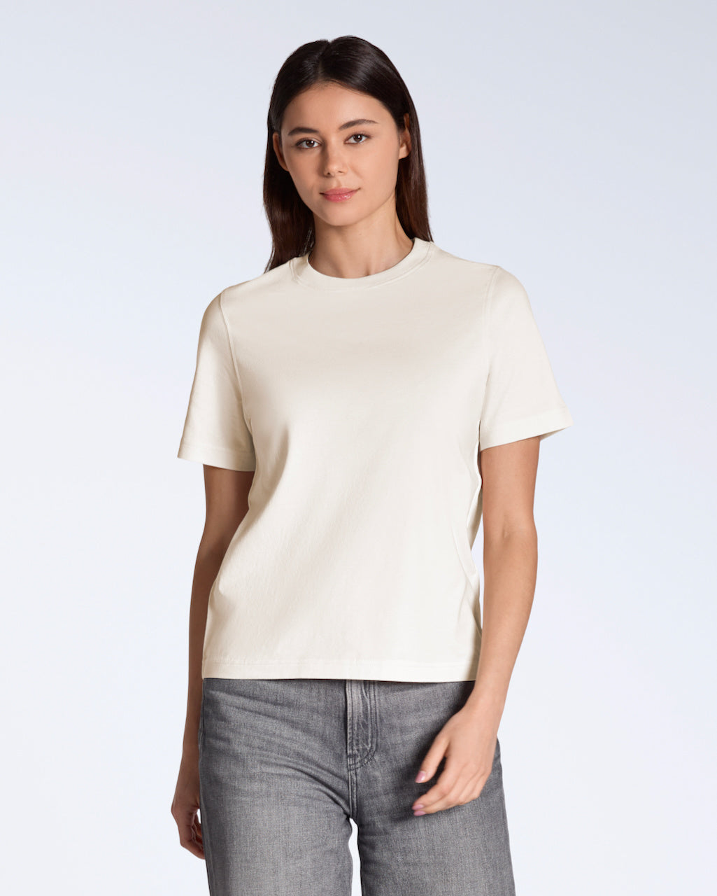 A woman looking into the camera, modelling a plain natural coloured, organic cotton t shirt.