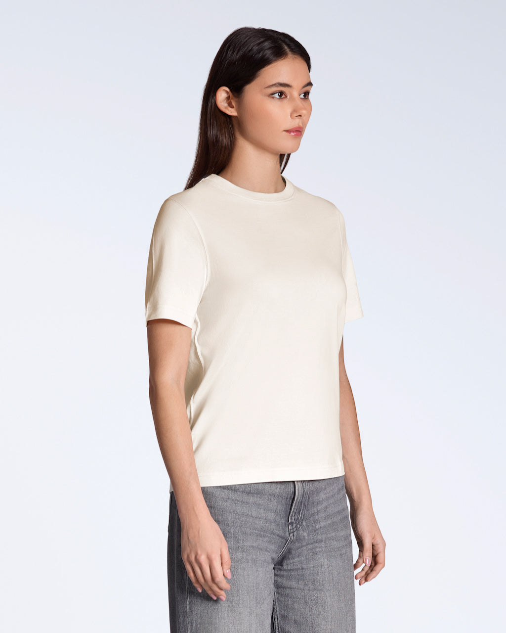 A woman at an angle to the camera with her arms by her side, modelling a plain natural coloured, organic cotton t shirt.
