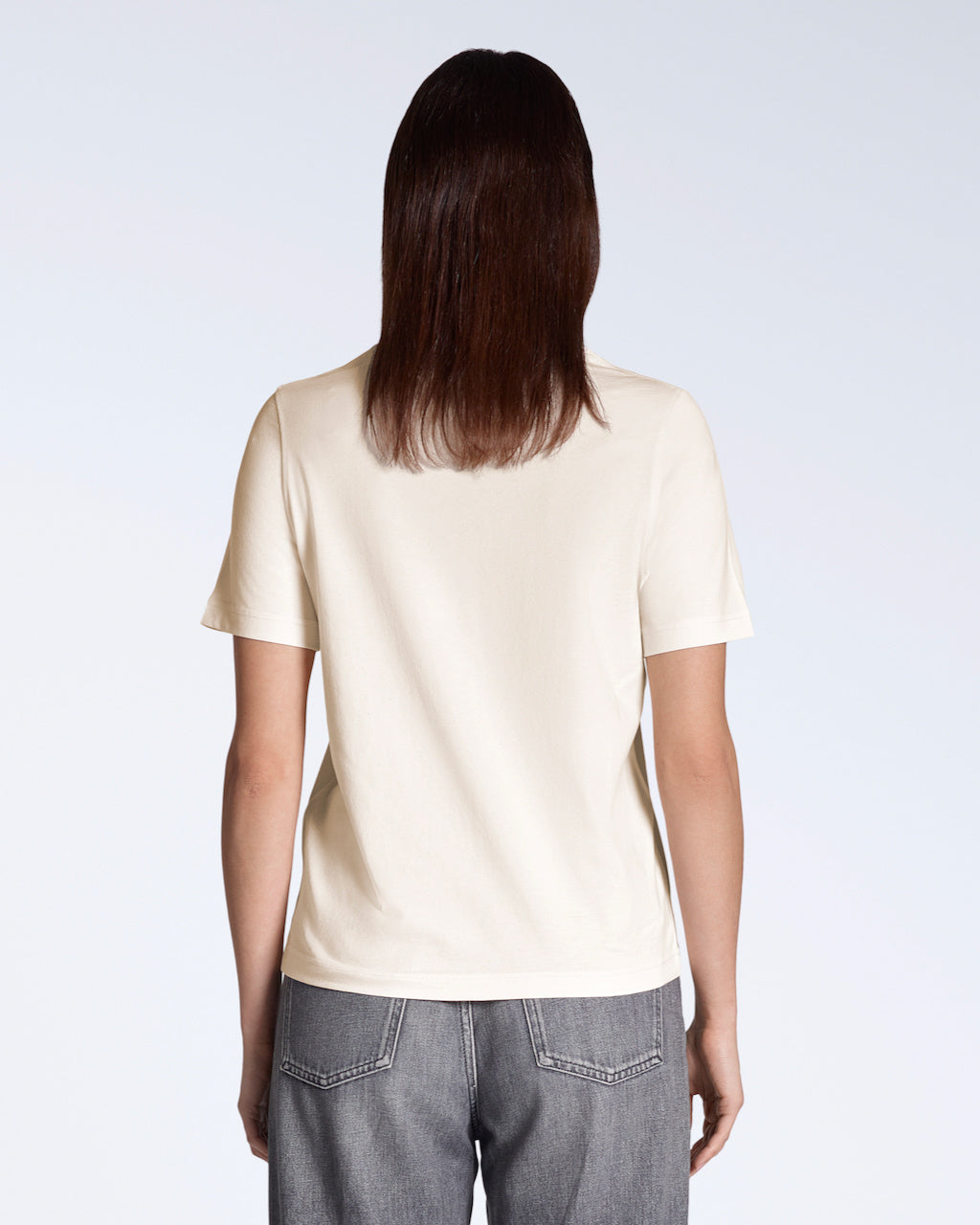A woman facing away from the camera, modelling a plain natural coloured, organic cotton t shirt.