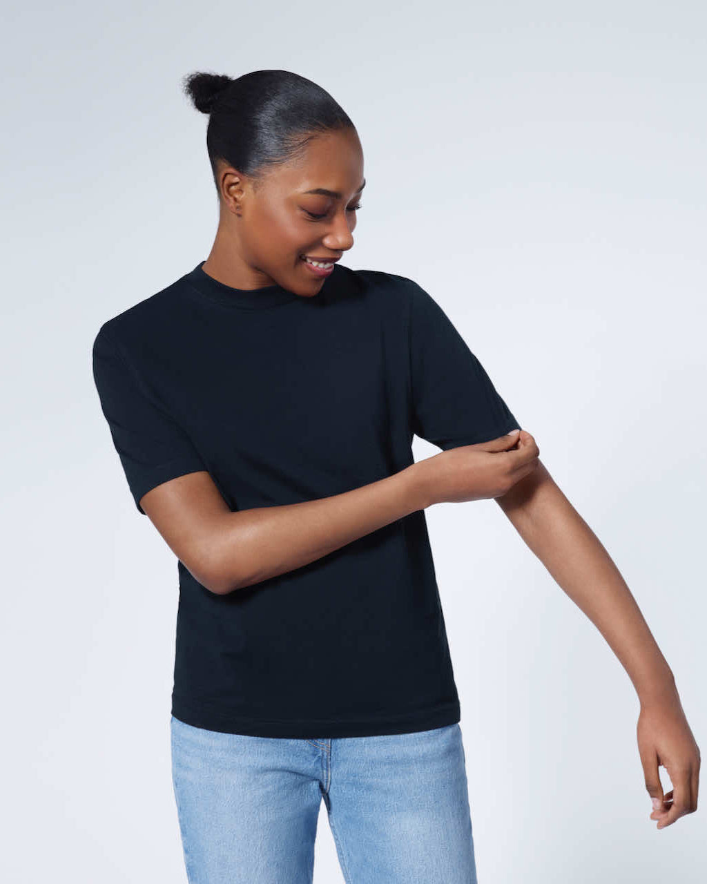 A woman looking down smiling and touching her sleeve, modelling a plain navy short sleeve organic cotton t shirt.