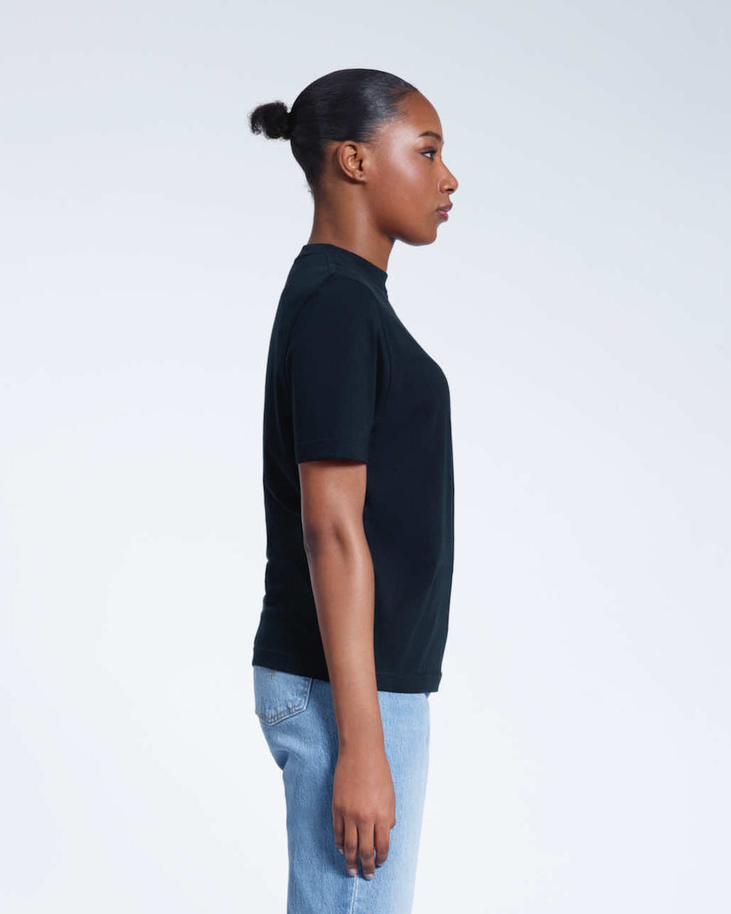 A woman facing side on, modelling a plain navy short sleeve organic cotton t shirt.