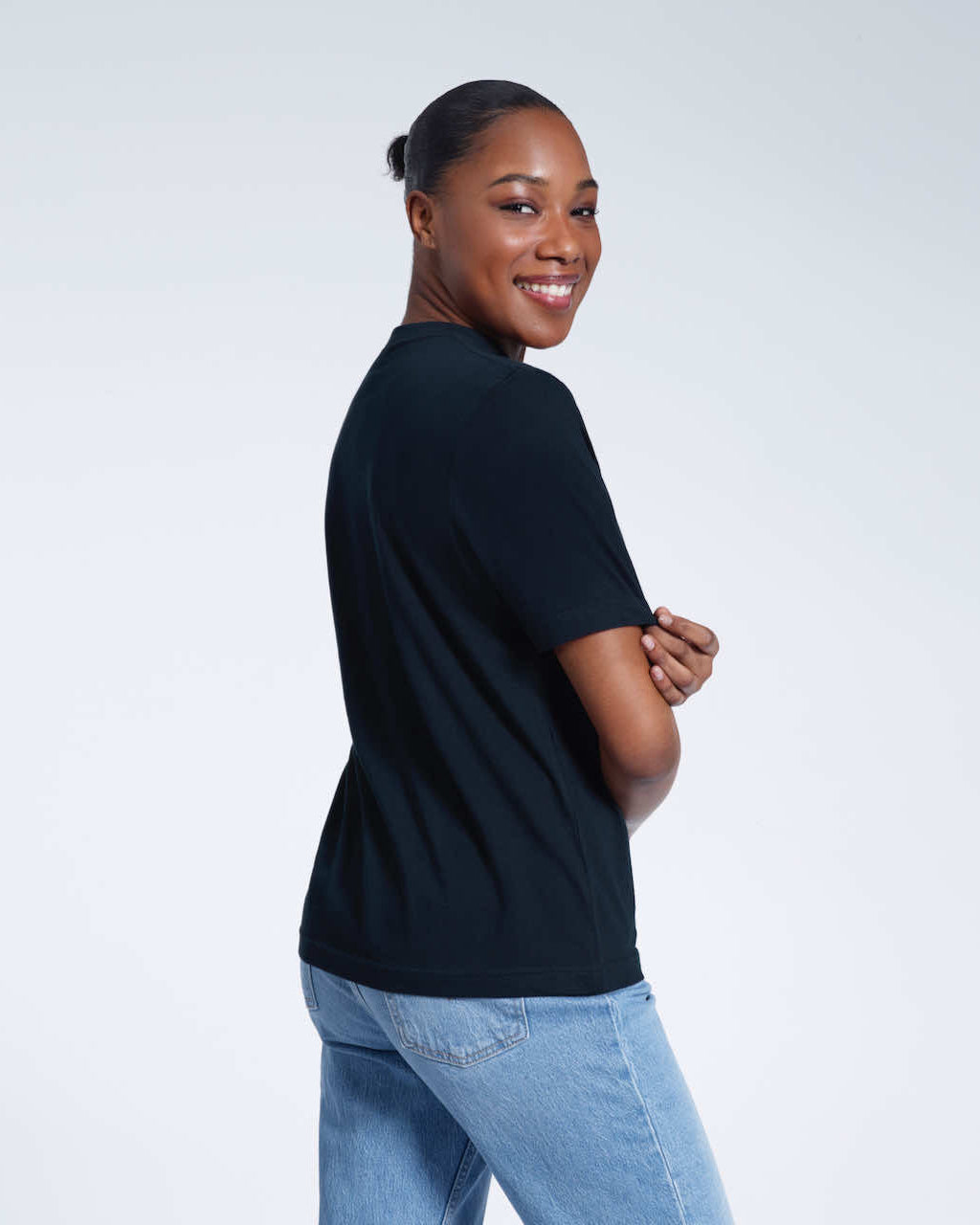 A woman turned towards the camera touching her sleeve smiling, modelling a plain navy short sleeve organic cotton t shirt.