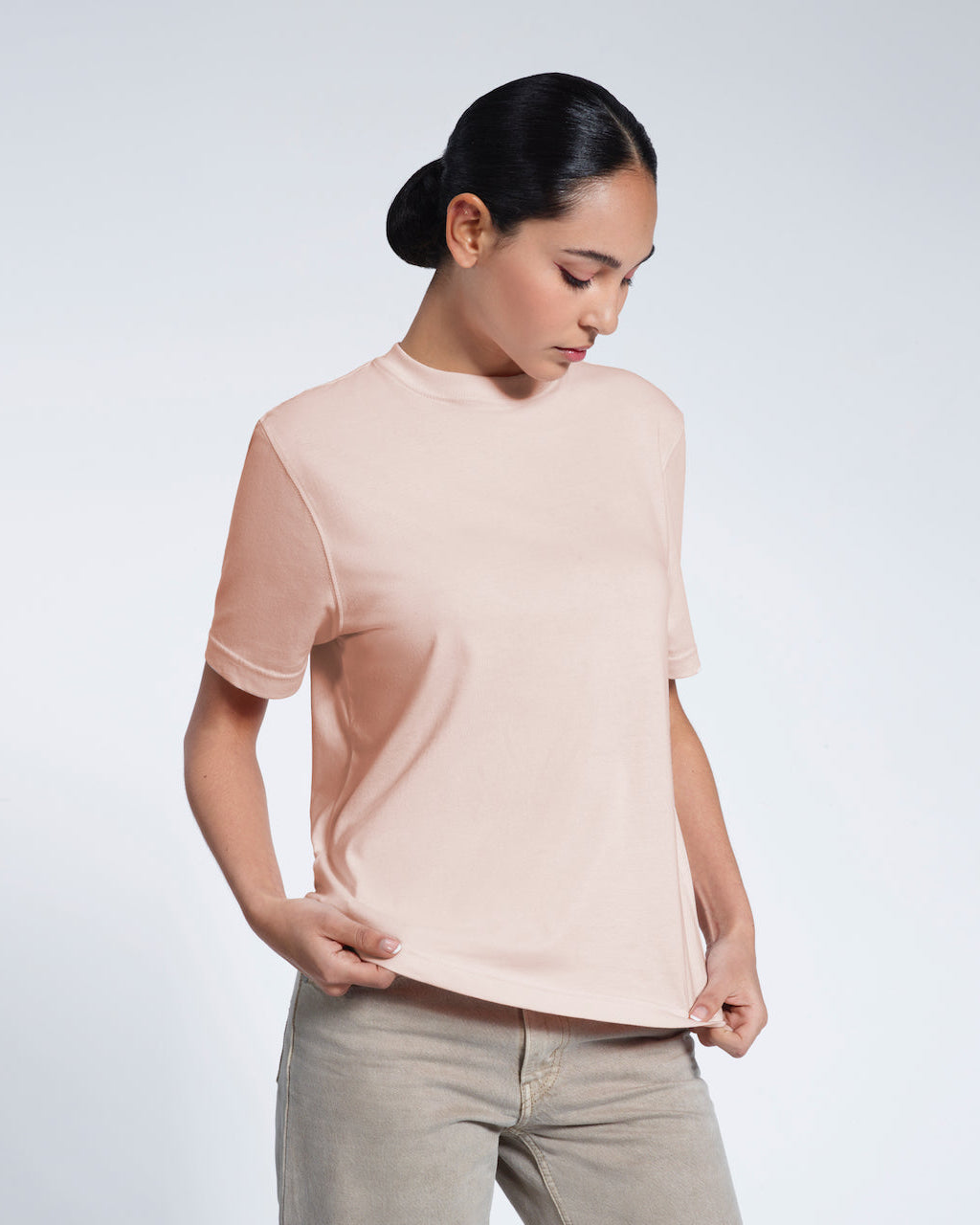 A woman looking down and touching the bottom of her plain pink short sleeve organic cotton t shirt.