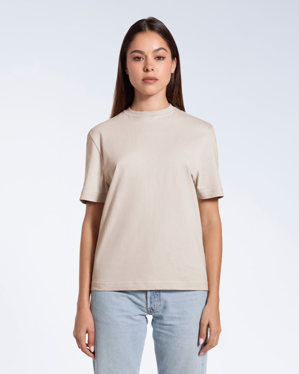 A woman facing front on looking at the camera, modelling a stone coloured short sleeve organic cotton t shirt.