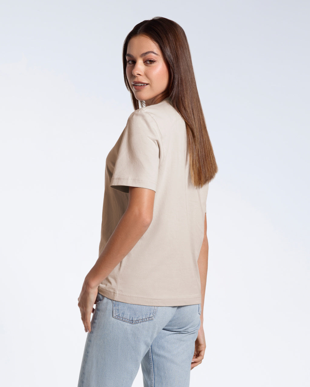 A woman turned towards the camera smiling, modelling a plain stone coloured short sleeve organic cotton t shirt.