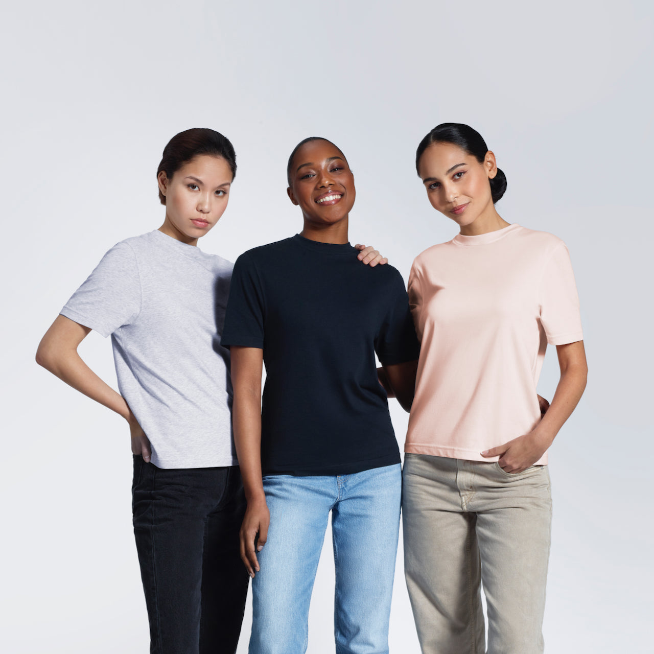 Three women looking into the camera, modelling plain grey, navy and pink organic cotton crew neck t shirts.