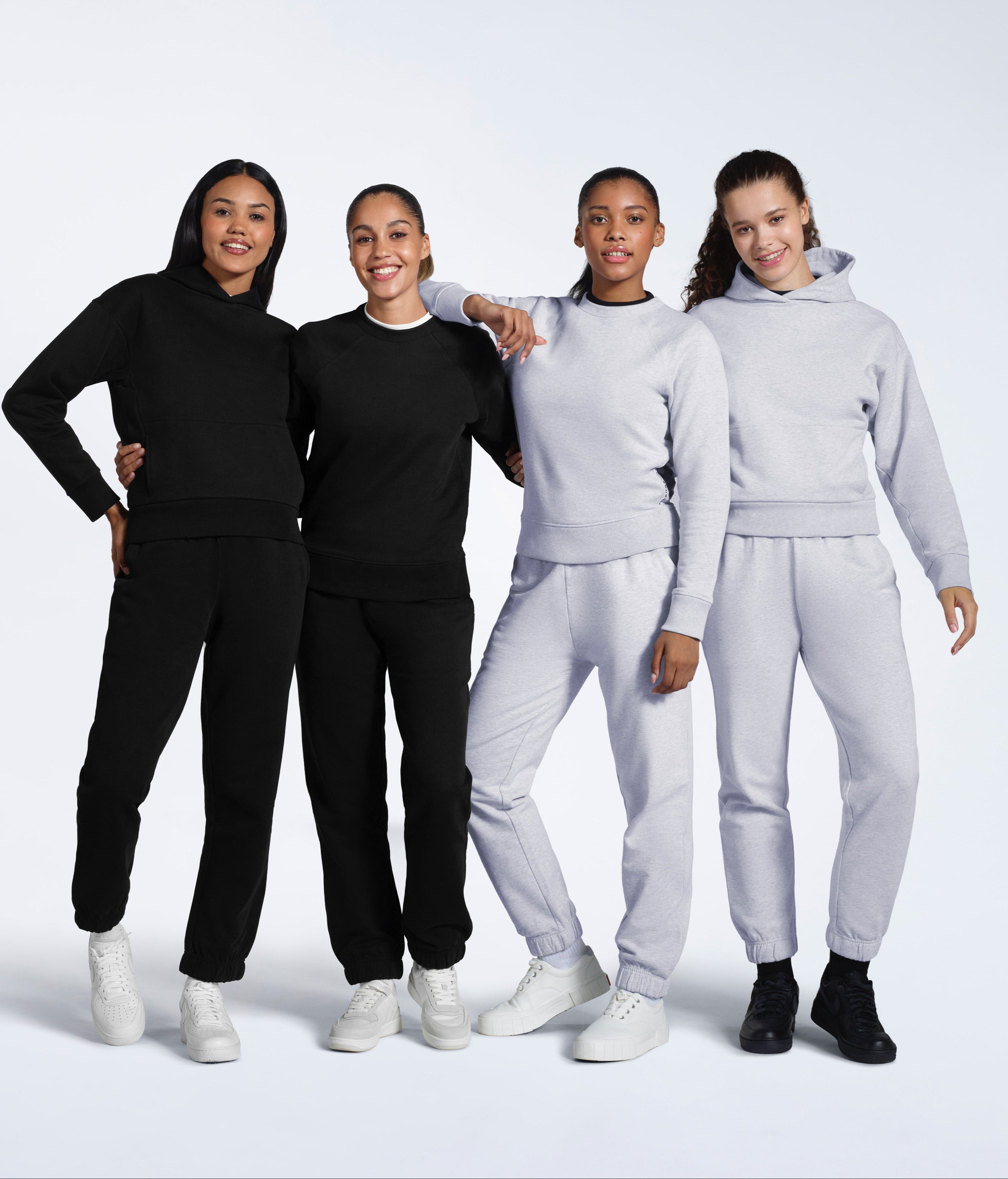 Four women smiling, modelling plain black and grey matching heavyweight organic cotton tracksuits.