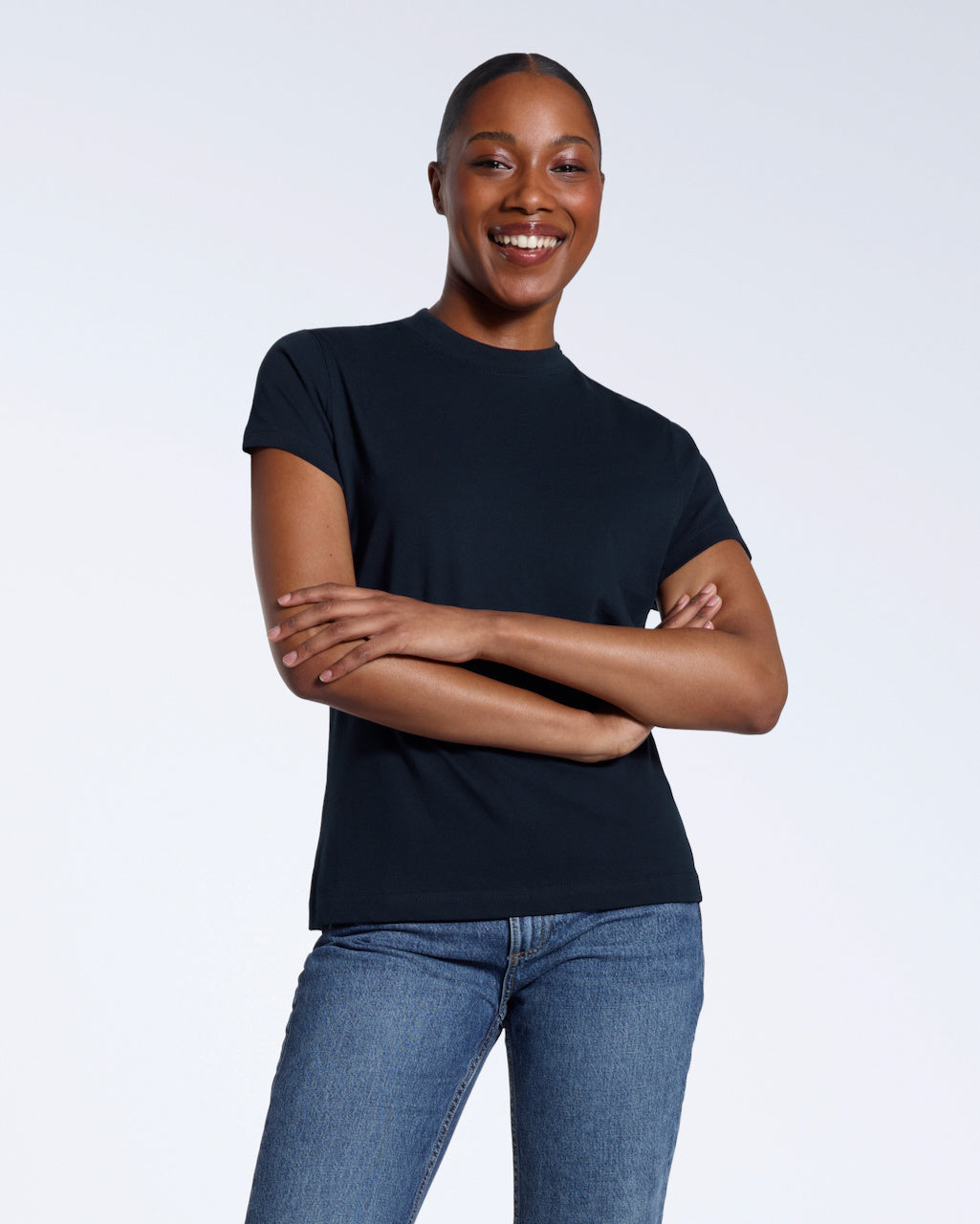A woman smiling into the camera with her arms folded, modelling a plain navy short sleeve organic cotton t shirt.