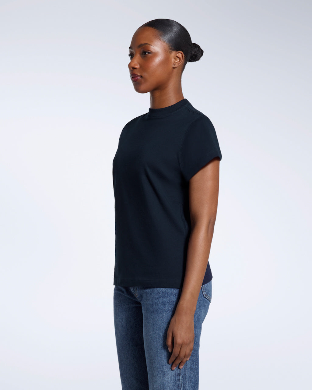 A woman looking away from the camera with her arms by her sides, modelling a plain navy short sleeve organic cotton t shirt.