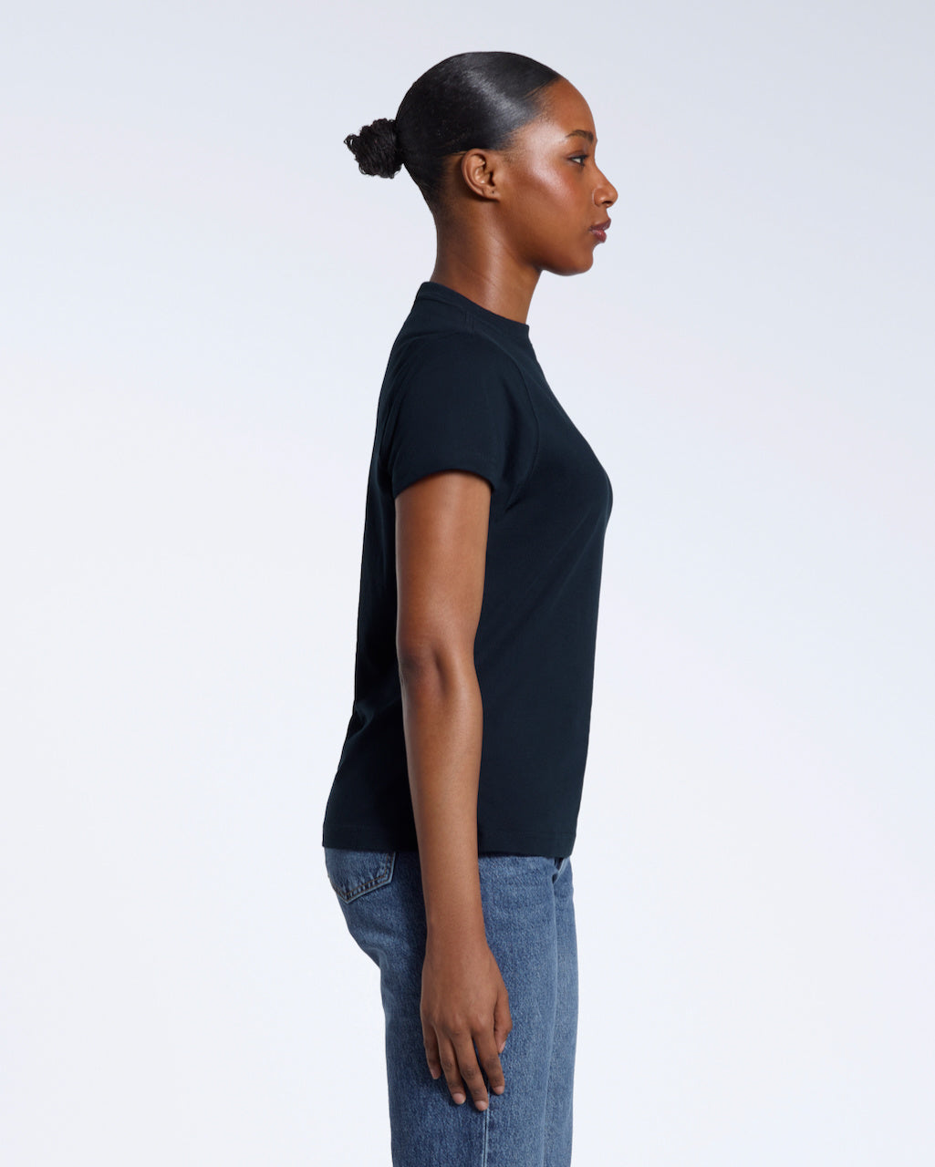 A woman facing side on with her arms by her sides, modelling a plain navy short sleeve organic cotton t shirt.