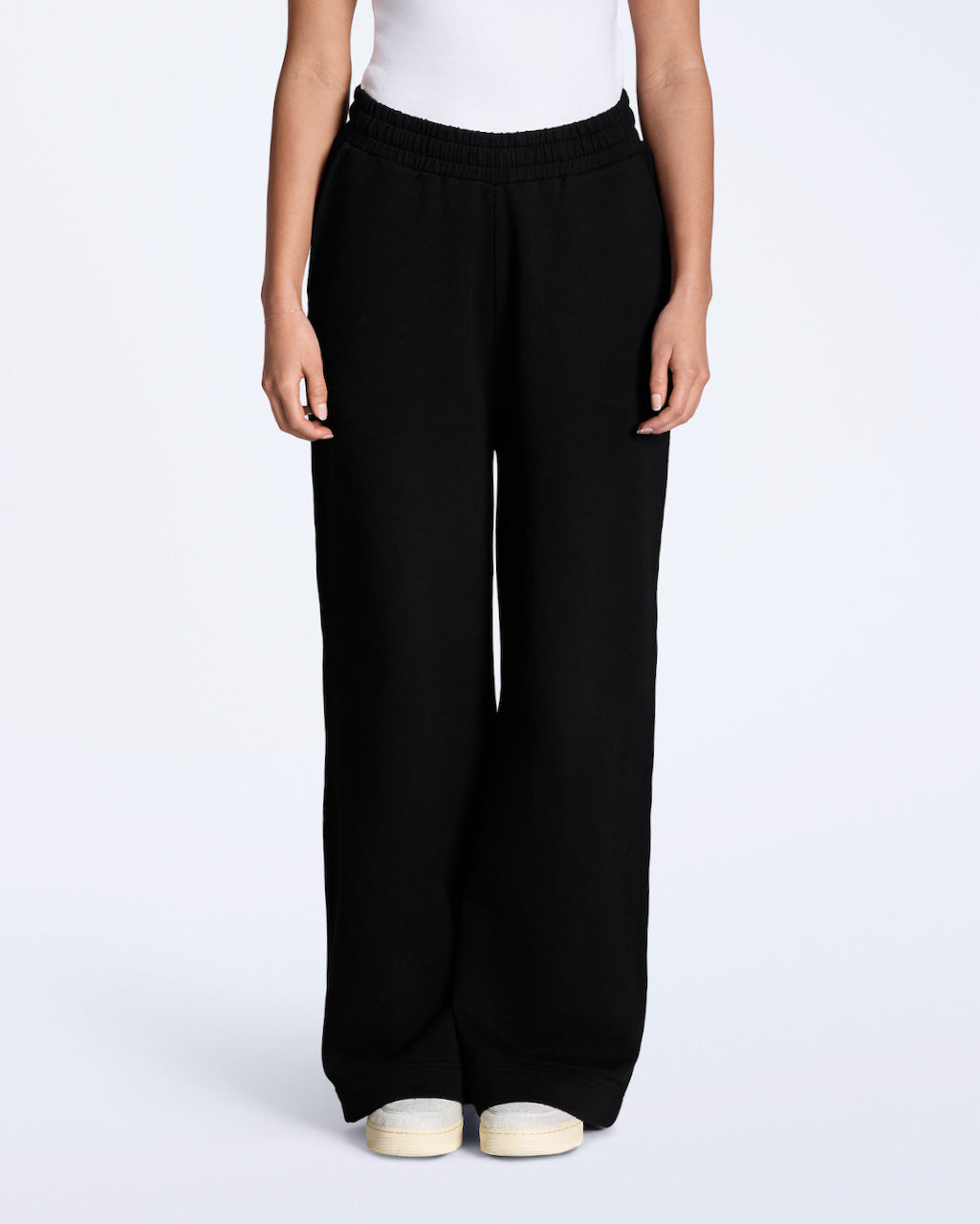 A woman facing front on with her hands by her sides, modelling a pair of black, organic cotton, wide leg joggers.