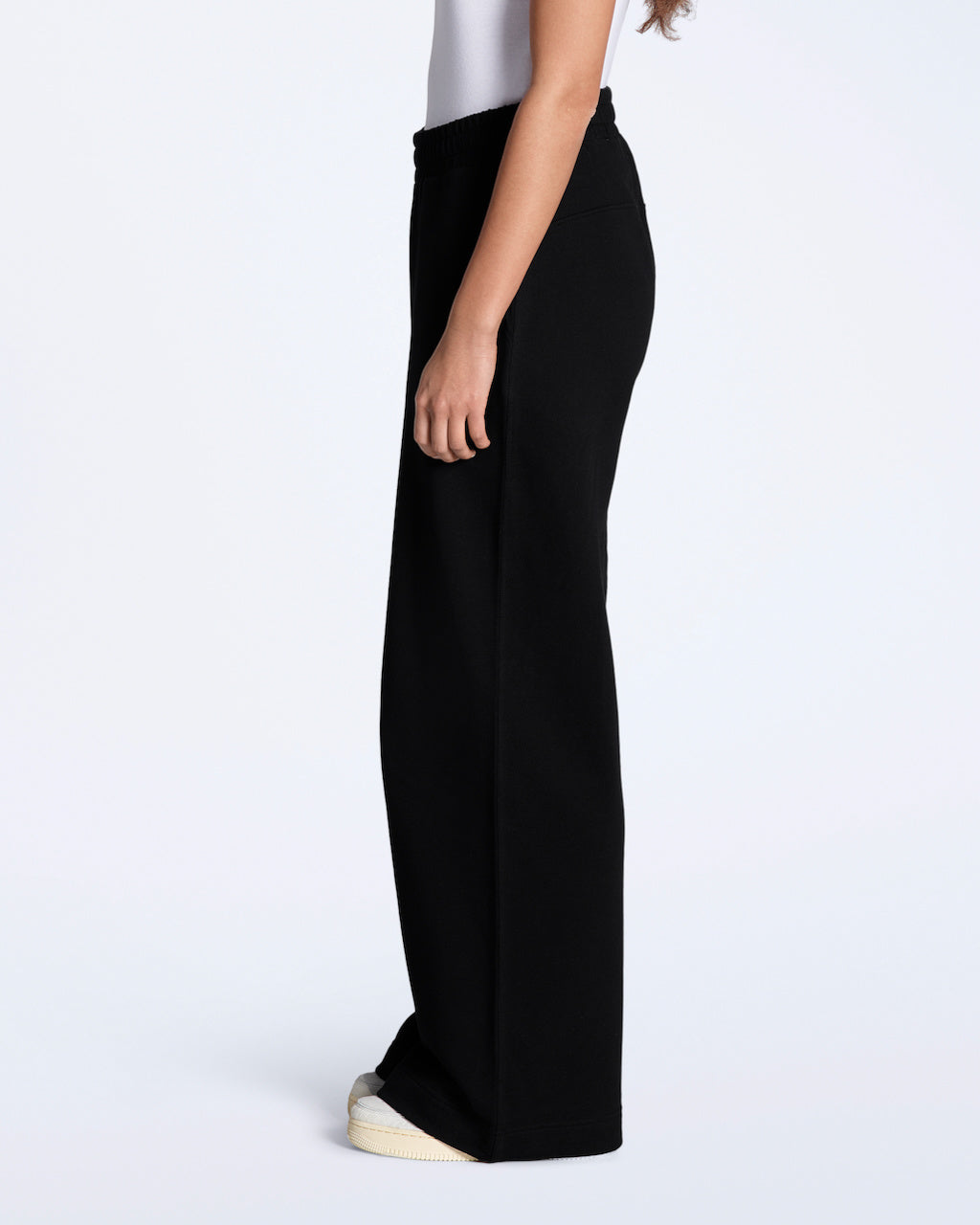 A woman facing side on with her hands by her sides, modelling a pair of black, organic cotton, wide leg joggers.