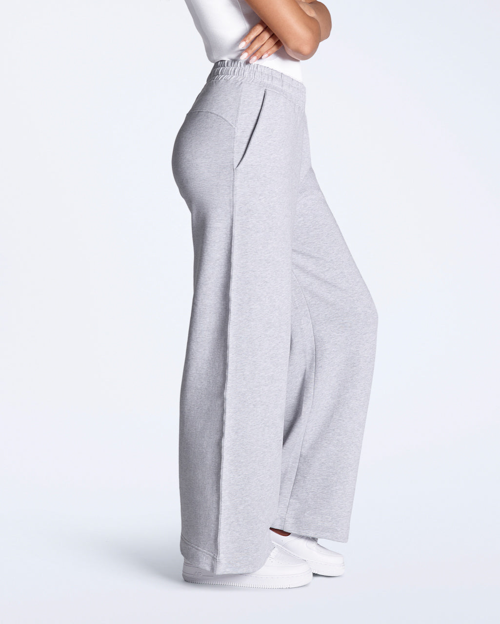 A woman facing side on with her arms crossed, modelling a pair of grey, wide leg, organic cotton joggers.
