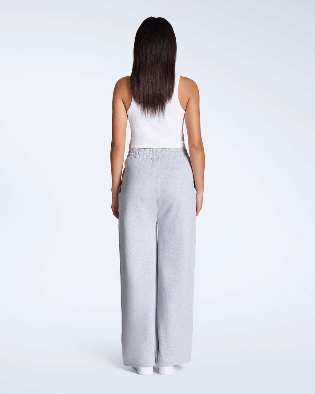 A woman facing away from the camera with her hands by her sides, modelling a pair of grey, organic cotton, wide leg joggers.