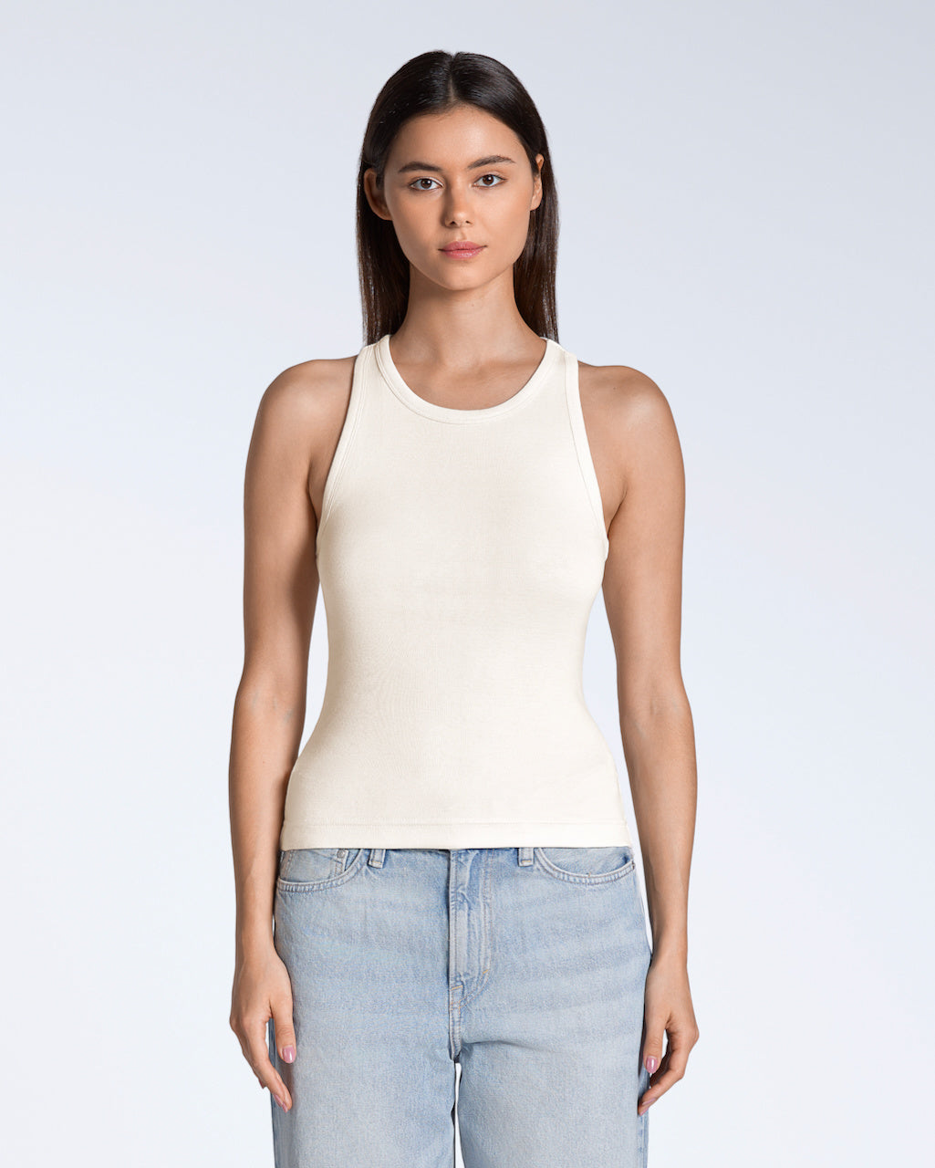 A woman facing front on, modelling a plain natural coloured, organic cotton tank top.