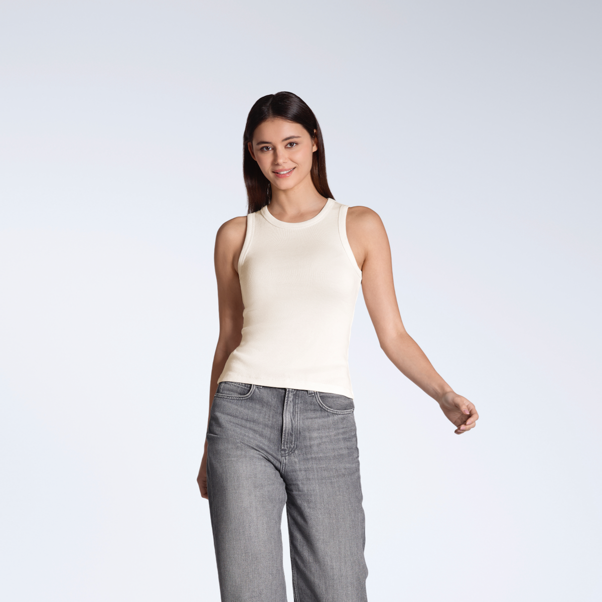 A woman smiling into the camera, modelling a plain natural coloured, organic cotton tank top.