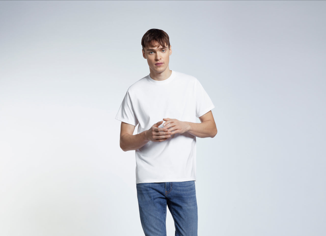 A man with his hands together looking into the camera, modelling a plain white short sleeve organic cotton t shirt.