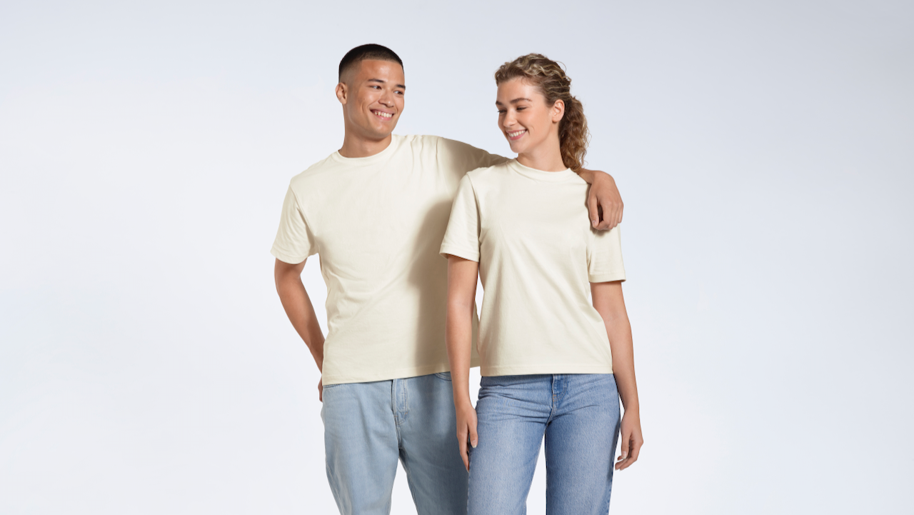 A man and woman smiing at eachother, modelling matching plain, ecru, organic cotton t shirts.