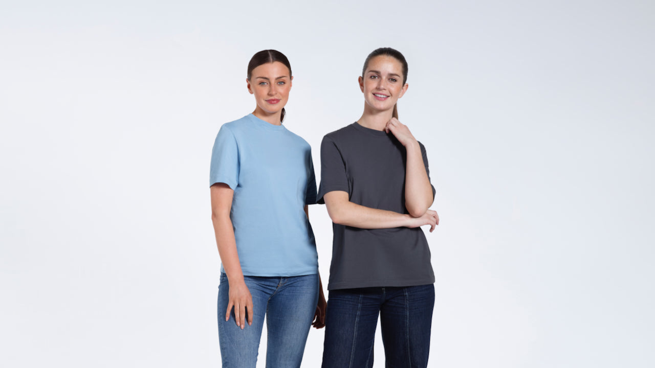 Two women smiling at the camera, modelling plain blue and dark grey organic cotton t shirts.