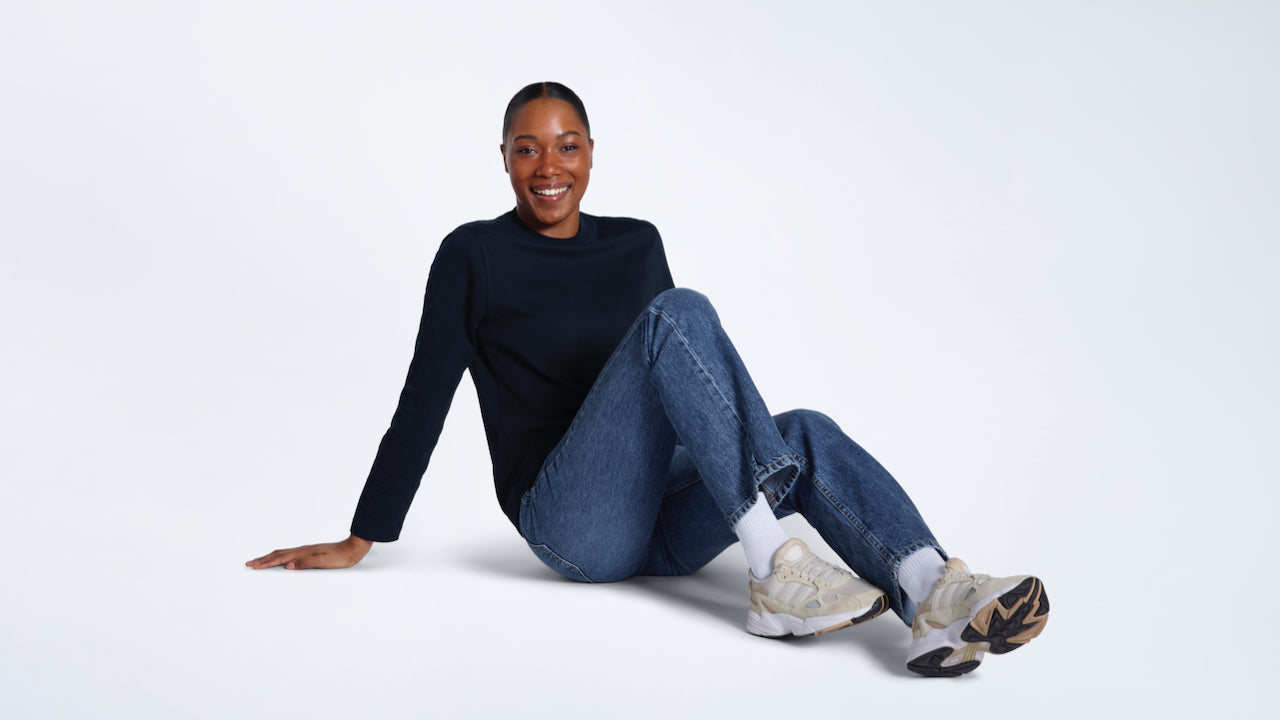 A woman sitting on the floor smiling, modelling a plain navy long sleeve organic cotton t shirt.