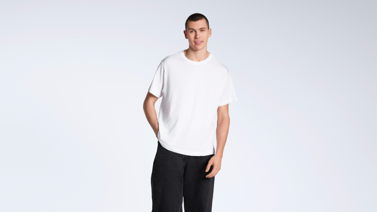 A man smiing into the camera with a hand in his pocket, modelling a plain white, organic cotton t shirt with a pair of black jeans.