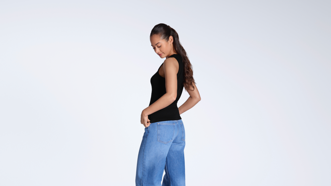 A woman looking down at her top, modelling a plain black, organic cotton tank top.