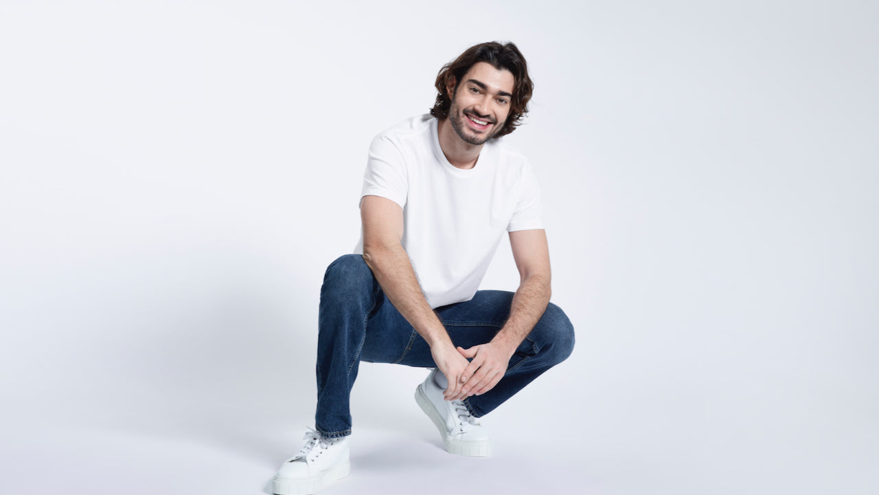 A man crouching down smiling, modelling a plain white short sleeve organic cotton t shirt.